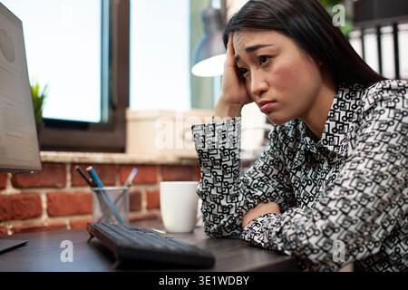 Primo piano di un'imprenditrice esausta che riposa il viso sul palmo della scrivania dopo una lunga giornata di lavoro. Donna d'affari con la mano sulla fronte che cerca di rimanere vigile mentre lavora al computer in un ufficio di avvio. Foto Stock