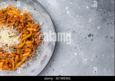 Abbondante pasta alla bolognese italiana condita con salsa di carne macinata e formaggio grattugiato su un piatto di ceramica grigia su fondo in pietra Foto Stock