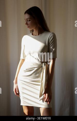 Donna alla moda in abito a manica lunga off-White aderente con nodo in vita: Elegante stile minimal e moderno concetto di stile di vita Foto Stock