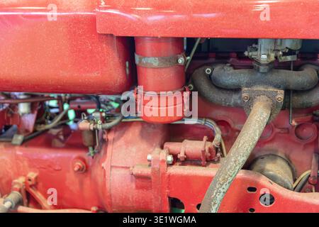 Un'immagine ravvicinata rivela il motore di un trattore rosso che mostra i tubi e i componenti meccanici applicazioni meccaniche o industriali agricole. Foto Stock