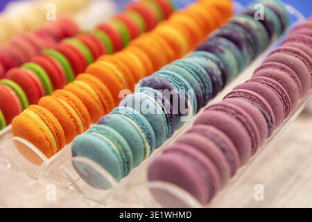 Vengono visualizzate file di macaron colorati, tra cui rosso arancione blu e viola. Questi macaron sono concetti di pasticceria, panetteria e dessert. Foto Stock