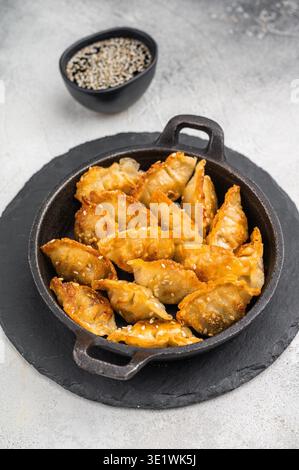 Gnocchi fritti dorati jiaozi cosparsi di sesamo serviti in padella nera su una superficie di pietra brillante, perfetto spuntino asiatico Foto Stock