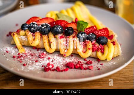 Pancake con mirtilli e fragole a fette decorato con crema di vaniglia su piatto grigio. Foto Stock