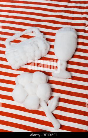 I morbidi bastoncini di cotone bianco poggiano su un tessuto a righe rosso-bianco. Un bocciolo a forma di cesto, un altro a forma di calice. Il terzo bocciolo forma un delicato fiore Foto Stock