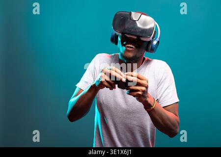 Gamer con occhiali VR e controller, completamente impegnato in videogame futuristici con il gioco online. Uomo felice in piedi in studio, con cuffie wireless, giochi con un'esperienza visiva 3D. Foto Stock