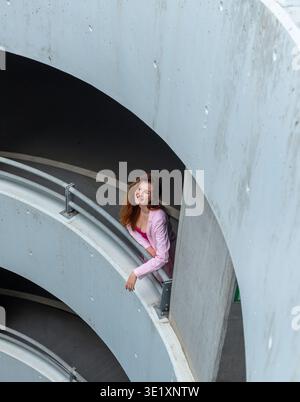 Una giovane donna sorridente che si gode una pausa nel parcheggio, sopra la vista Foto Stock