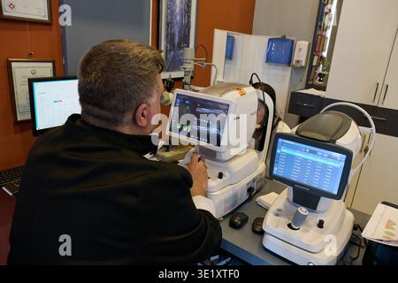 Oftalmologo maschile che esegue una scansione retinica utilizzando una moderna macchina OCT Huvitz per la diagnostica oculare e la tomografia a coerenza ottica in una clinica. Foto Stock