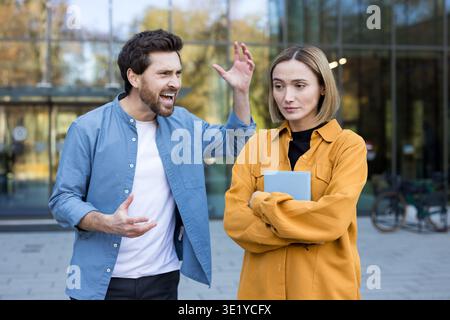 Uomo sconvolto con rabbia di fronte a una donna calma che tiene un libro, tesa disputa sul posto di lavoro che mostra urla, stress, interruzione della comunicazione, angoscia emotiva tra colleghi Foto Stock