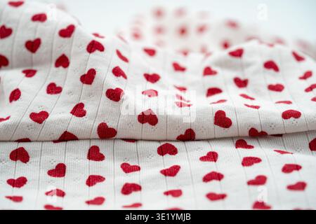 Primo piano di tessuto bianco con motivo a cuore rosso e texture tessile. Foto Stock