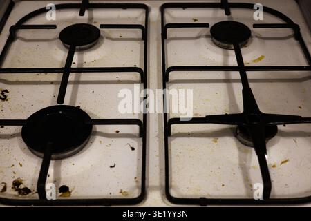 Un colpo top-down professionale di un piano cottura a gas bianco ricoperto da schizzi di grasso, particelle di cibo essiccate e macchie. L'immagine acquisisce lo stato di A. Foto Stock
