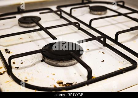 Un colpo top-down professionale di un piano cottura a gas bianco ricoperto da schizzi di grasso, particelle di cibo essiccate e macchie. L'immagine acquisisce lo stato di A. Foto Stock