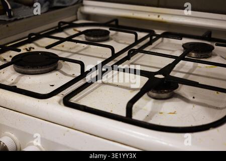 Un colpo top-down professionale di un piano cottura a gas bianco ricoperto da schizzi di grasso, particelle di cibo essiccate e macchie. L'immagine acquisisce lo stato di A. Foto Stock