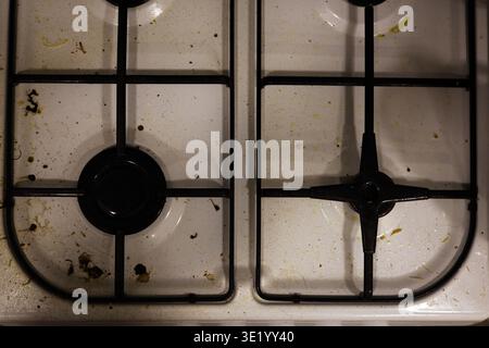 Un colpo top-down professionale di un piano cottura a gas bianco ricoperto da schizzi di grasso, particelle di cibo essiccate e macchie. L'immagine acquisisce lo stato di A. Foto Stock