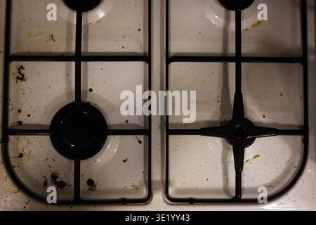 Un colpo top-down professionale di un piano cottura a gas bianco ricoperto da schizzi di grasso, particelle di cibo essiccate e macchie. L'immagine acquisisce lo stato di A. Foto Stock