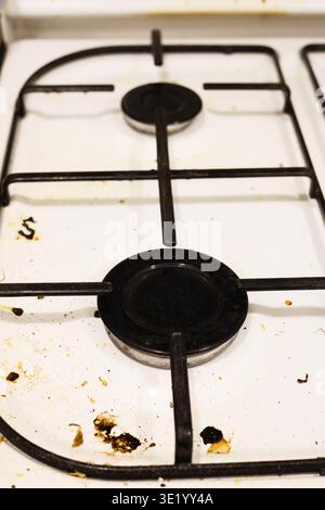 Un colpo top-down professionale di un piano cottura a gas bianco ricoperto da schizzi di grasso, particelle di cibo essiccate e macchie. L'immagine acquisisce lo stato di A. Foto Stock