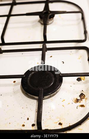 Un colpo top-down professionale di un piano cottura a gas bianco ricoperto da schizzi di grasso, particelle di cibo essiccate e macchie. L'immagine acquisisce lo stato di A. Foto Stock