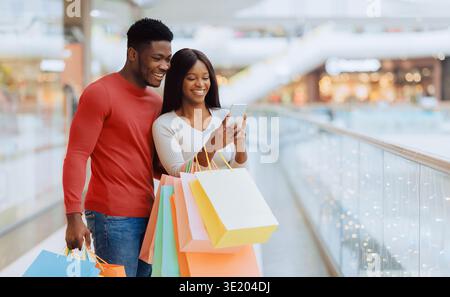 La coppia ama fare shopping e guardare il proprio telefono cellulare in un centro commerciale durante il giorno Foto Stock
