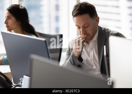 Uomo d'affari di mezza età che pensa per schermo al computer sul posto di lavoro Foto Stock