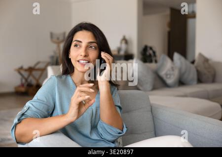 Donna brasiliana che parla con uno smartphone seduto in un ambiente accogliente Foto Stock