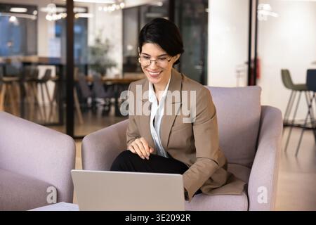 Donna d'affari caucasica sorridente che lavora su un computer portatile seduto nella sala dell'ufficio Foto Stock
