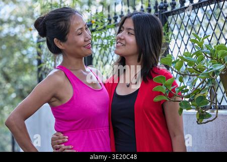 Le amiche con abiti rosa e rosso avvolgono l'aria calda all'aperto, un momento di riunione felice Foto Stock