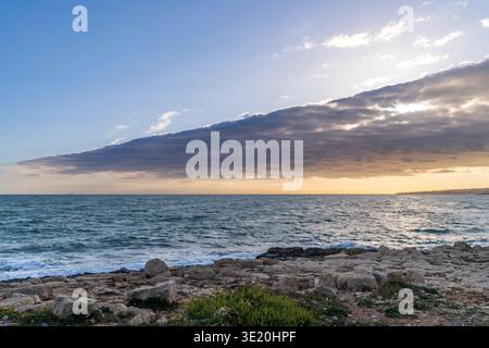 Vista suggestiva di Punta Pisciotto a Sampieri, Sicilia. L'immagine cattura le scogliere calcaree lambite dal Mar Mediterraneo sotto un cielo spettacolare Foto Stock