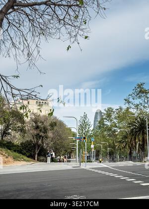 BARCELLONA, SPAGNA - 13 APRILE 2025: Scena di strada nel quartiere Poblenou di Barcellona con Torre Glories sullo sfondo sopra alberi, marciapiedi e strade Foto Stock