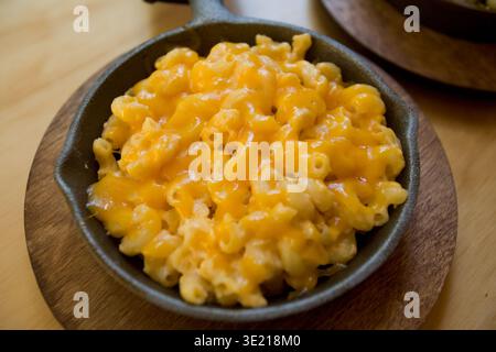 Macaroni cremosi e formaggio serviti in una padella di ghisa su un asse di legno. Foto Stock