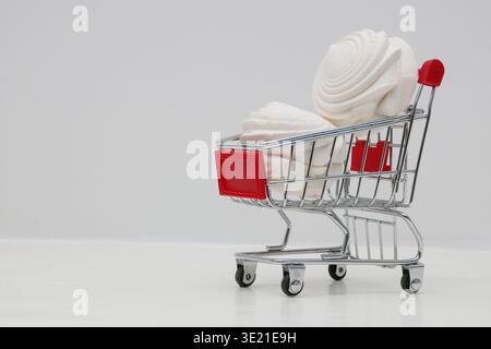 Marshmallow bianchi, meringhe in un carrello da supermercato su sfondo bianco, concetto commerciale, marketing. Foto Stock