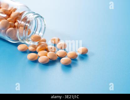 Vitamine arancioni o compresse integrative che fuoriescono da un flacone di vetro su sfondo blu con spazio di copia Foto Stock