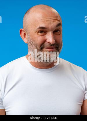 L'uomo sorride su un solido sfondo blu e indossa una camicia bianca Foto Stock