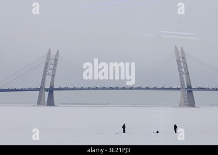 Pesca sul ghiaccio per tre persone vicino al grande ponte sospeso durante il giorno d'inverno Foto Stock