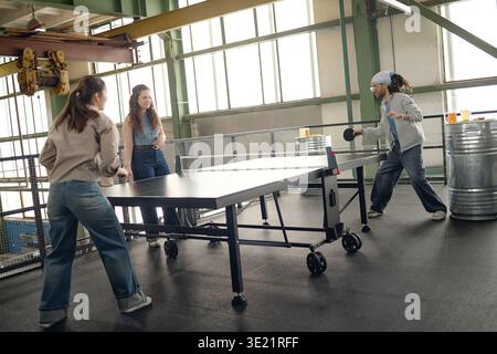 Giovani donne multietniche che giocano a ping pong nel moderno spazio di lavoro industriale Foto Stock