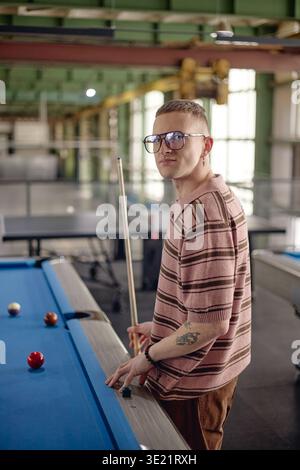 Ritratto verticale di un giovane adulto che gioca a biliardo in ambiente industriale Foto Stock