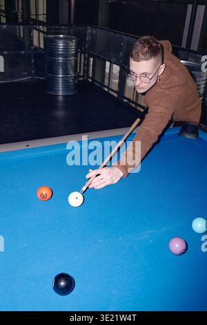 Vertical of Young Man che gioca a biliardo mentre punta Cue Ball sul tavolo da biliardo Foto Stock