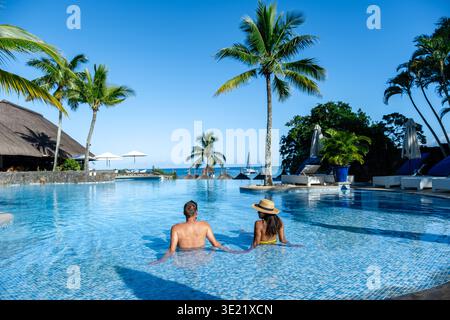 La coppia si rilassa in una splendida piscina a sfioro circondata da palme, godendosi la brezza tropicale e la vista mozzafiato dell'oceano a Mauritius. Una fuga perfetta per romanticismo e svago. Foto Stock