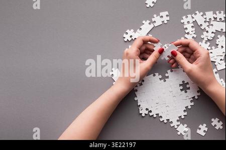 Pezzi del puzzle disposti su una superficie grigia con le mani che inseriscono un pezzo nel mosaico Foto Stock
