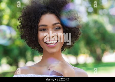 Donna afroamericana felice circondata da bolle nel parco Foto Stock
