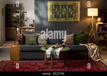 La scena del soggiorno mostra il tradizionale set da tè musulmano e dolci disposti su un tavolo rotondo di fronte al divano, tappeto a motivi geometrici e parete decorativa appesa sullo sfondo Foto Stock
