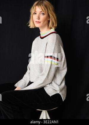Donna con i capelli biondi corti in un maglione grigio seduta su uno sgabello sullo sfondo nero. Germania Foto Stock