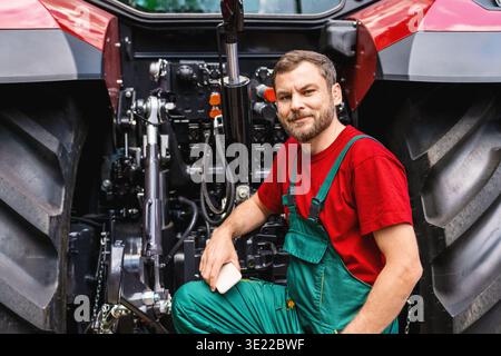 Meccanico delle macchine agricole appoggiato in modo uniforme su grandi ruote del trattore Foto Stock