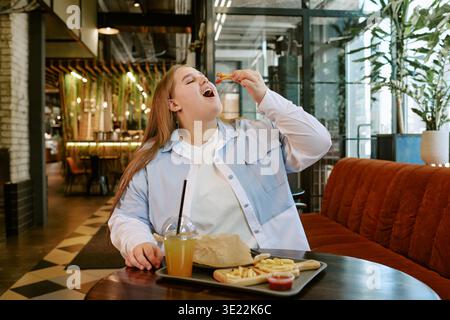 Giovane donna adulta che gusta il fast food nel ristorante moderno Foto Stock