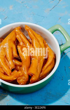 primo piano di alcuni piedi di pollo disossati asiatici ricoperti di gelatina in una casseruola di ceramica verde posta su un tavolo rustico blu Foto Stock