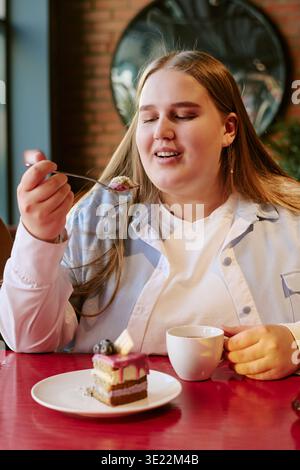 Ritratto di una giovane donna adulta che si gusta un dessert e beve un caffè Foto Stock