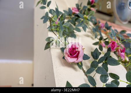 Un bellissimo fiore di rosa rosa artificiale con decorazioni a foglia verde dona un'atmosfera romantica e allegra agli spazi interni Foto Stock