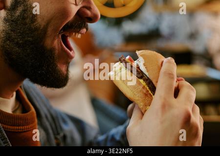 Giovane adulto che mangia hamburger al ristorante Smiling Foto Stock