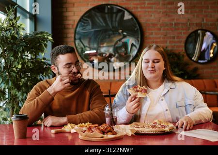 Giovane donna e giovane uomo che si godono mangiando pizza insieme al chiuso Foto Stock
