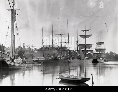 Questa fotografia antica di Barlow, probabilmente della fine degli anni '1800, cattura una scena movimentata al porto di Gustavsberg a Stoccolma, Svezia. Diverse navi a vela, tra cui navi a tre alberi, sono ormeggiate con edifici sulla riva che formano lo sfondo. L'immagine fornisce uno sguardo sulla storia industriale e marittima dell'area della fabbrica di porcellane di Gustavsberg. Foto Stock
