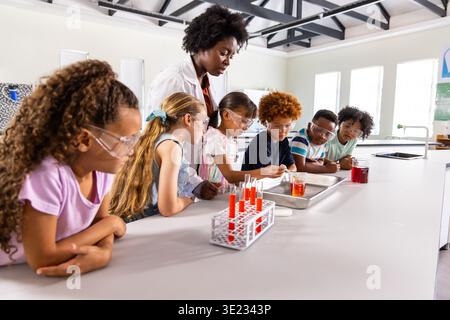 Insegnante senior afroamericano in camice da laboratorio che guida 6 bambini con gli occhiali, utilizzando la pipetta al banco del laboratorio Foto Stock