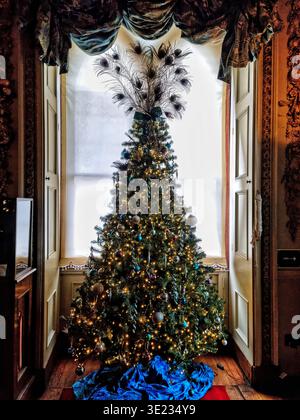 Elaborato albero di Natale all'interno del castello di Warwick decorato con piume di pavone, baubles ornati e spettacolare pennacchio in un ambiente storico festoso Foto Stock